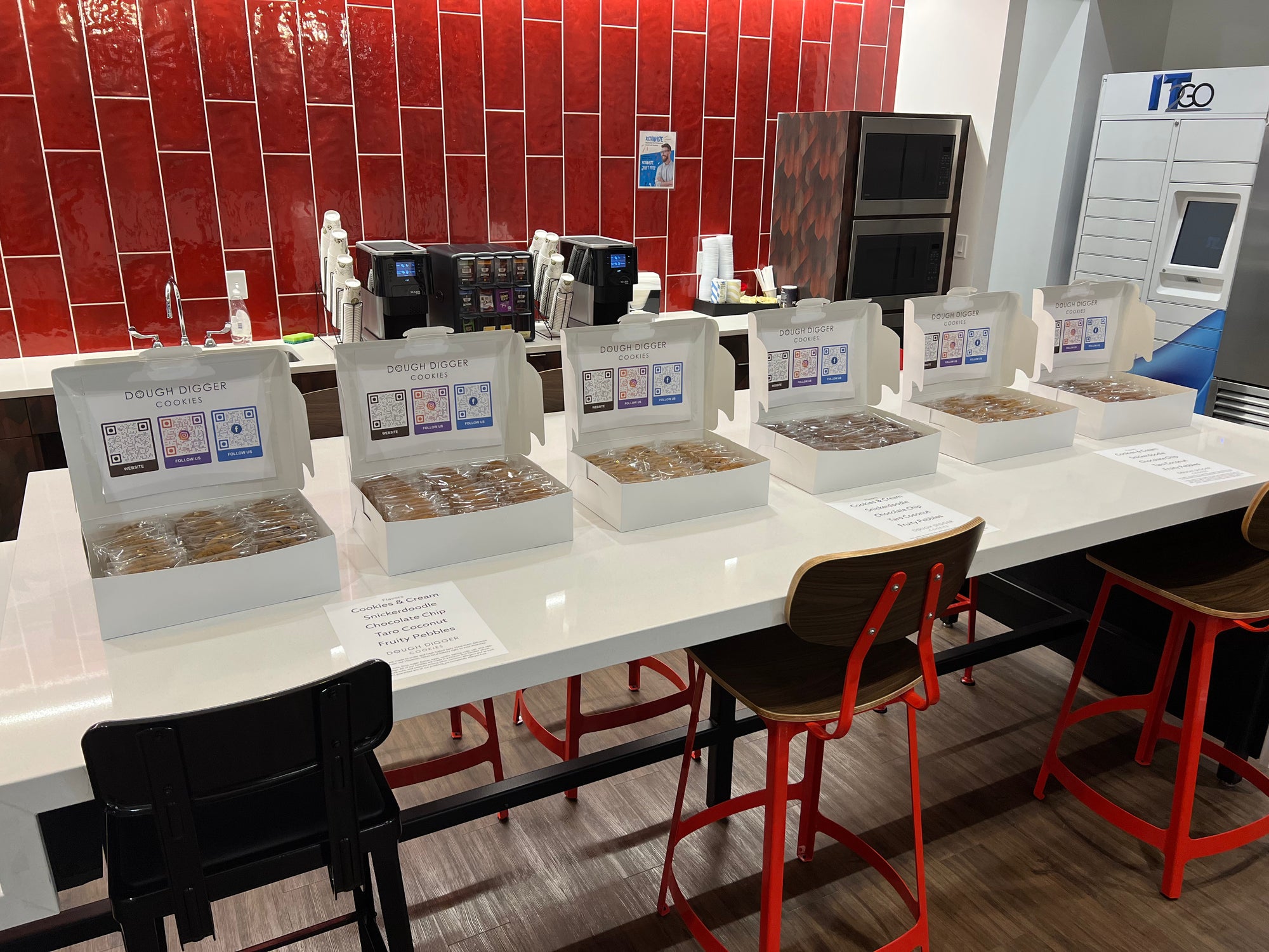 Six open boxes of individually wrapped cookies along an office counter, each lid showing a Dough Digger card with QR codes