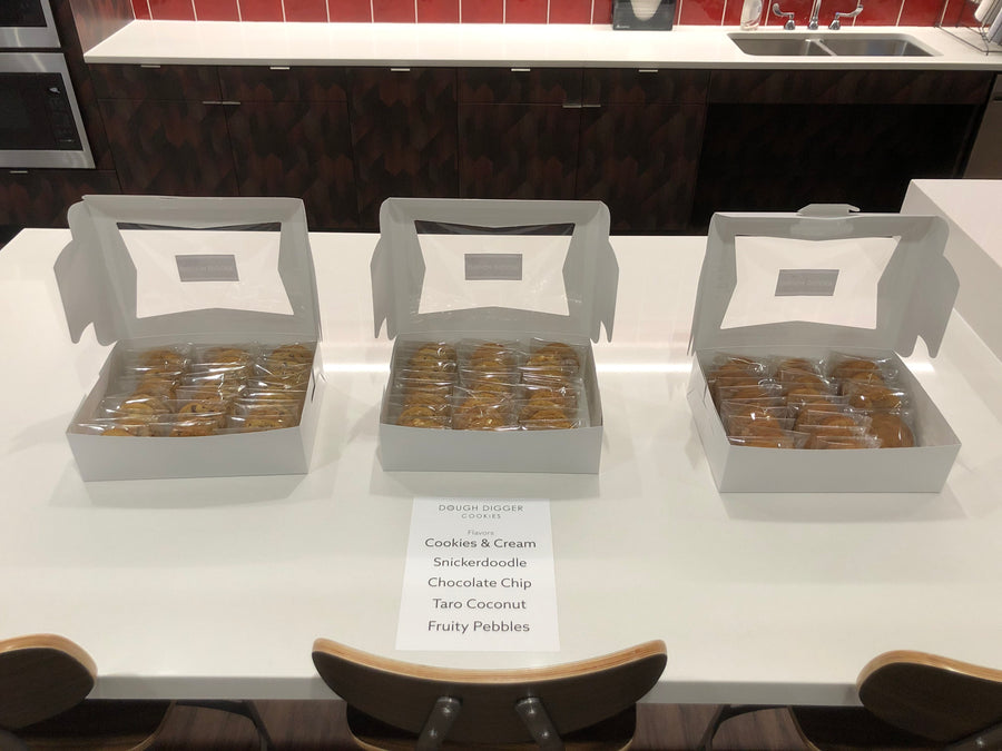 Three open boxes of individually wrapped cookies beside a printed Dough Digger flavor card
