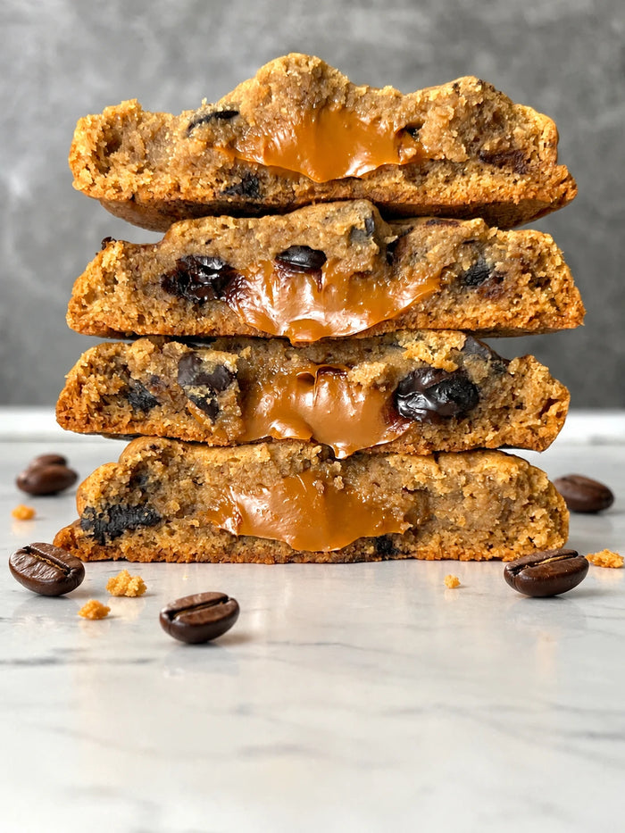 A stack of four Vietnamese Coffee cookies broken open with condensed milk filling, coffee beans scattered on the marble around them